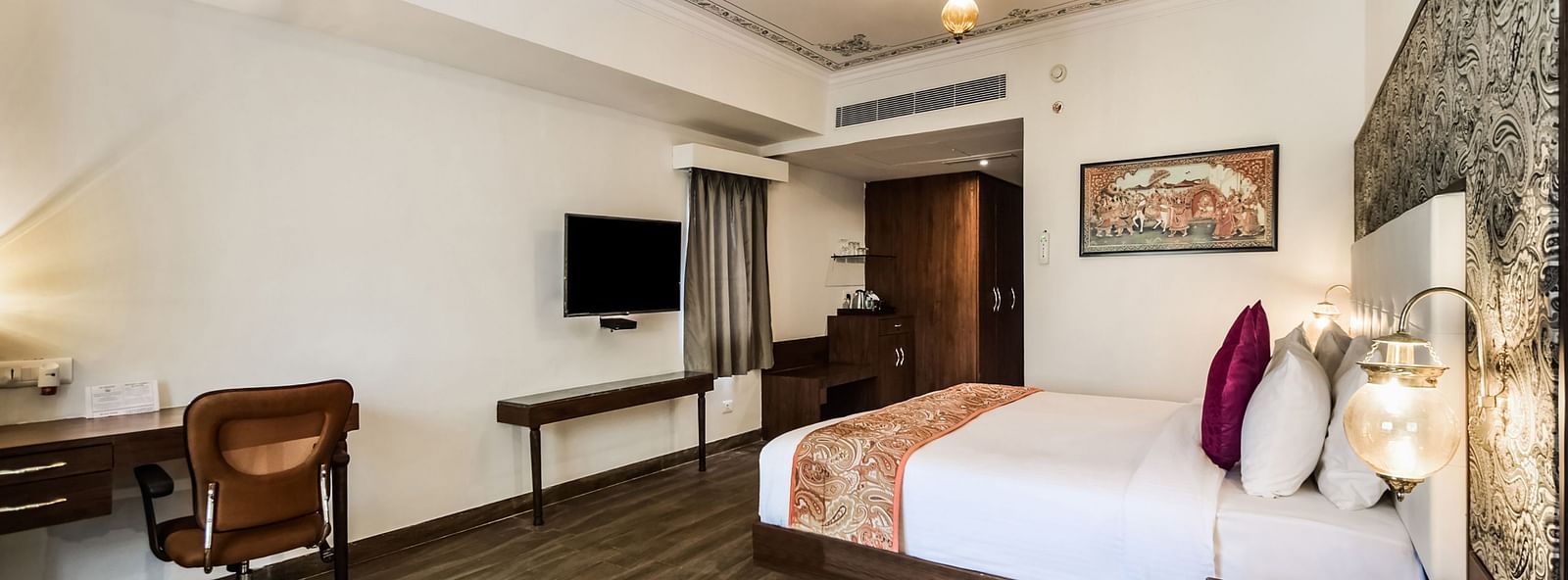  A hotel room with a large bed, a desk, and a seating area with warm lighting.- Bamboo Saa Resort & Spa, Udaipur