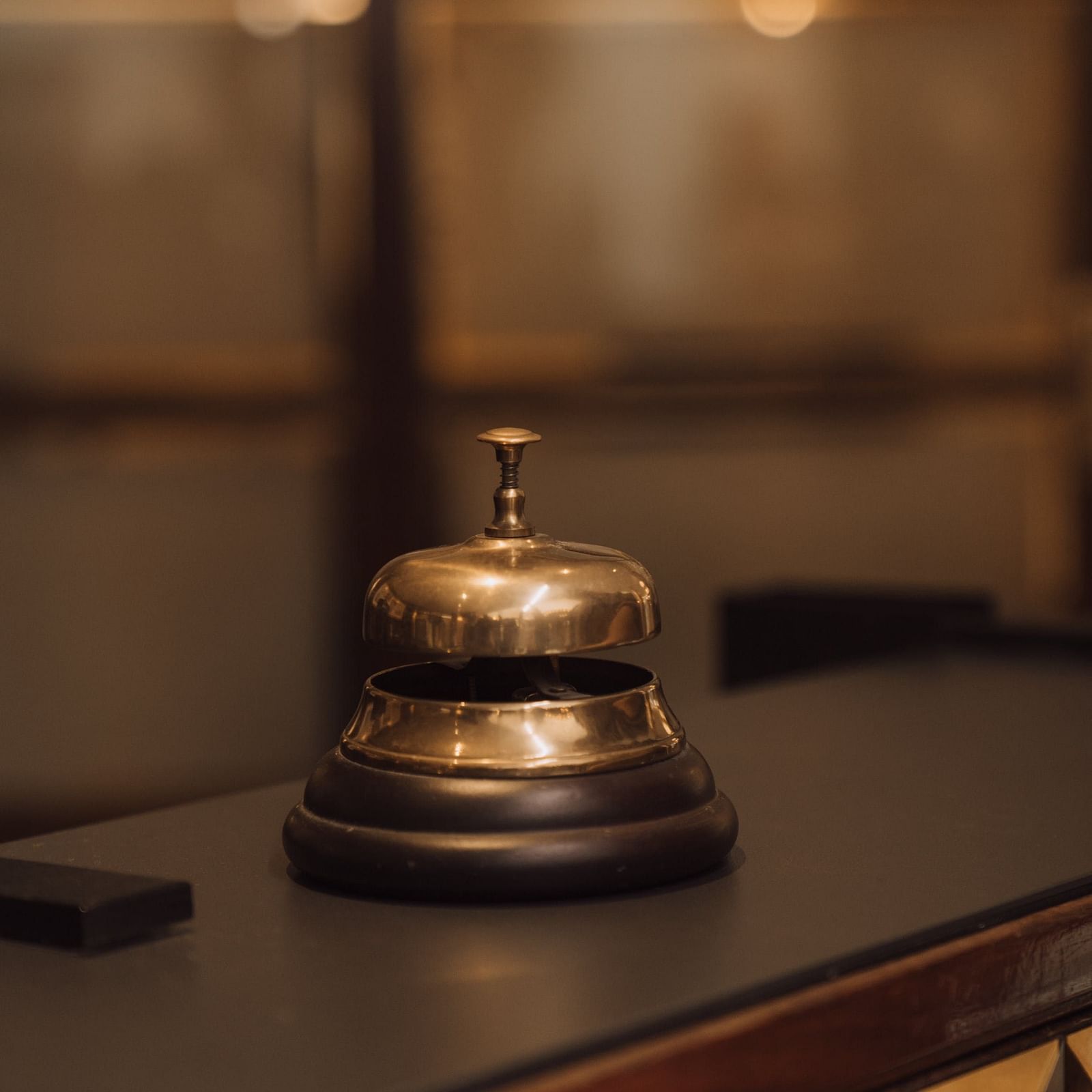 A close-up of a vintage service bell on a hotel reception desk with a blurred background