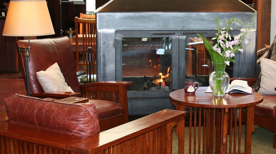 Lounge area with a red leather couch, a wooden table with flowers, and a glowing fireplace - Brewery Gulch Inn & Spa