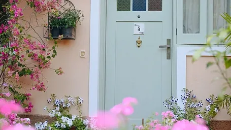 Entrance to a cottage at Karma Chalets, surrounded by pink flowers and potted plants.