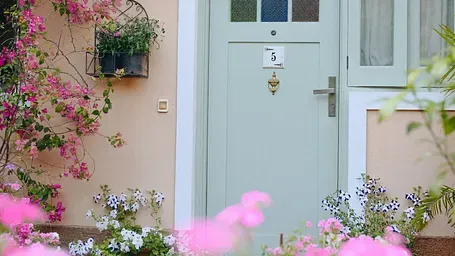 Entrance to a cottage at Karma Chalets, surrounded by pink flowers and potted plants.
