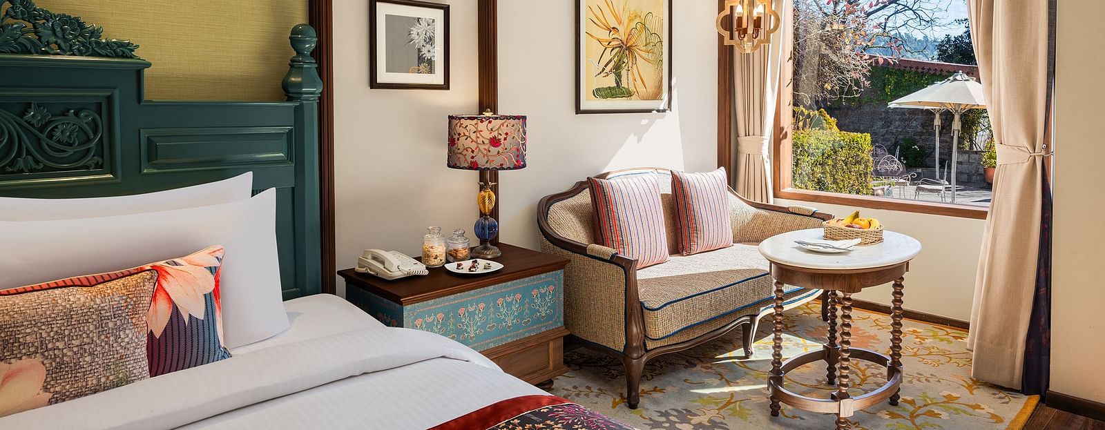 Premium Garden Room at naini retreat, nainital, A cozy and inviting hotel room with a king-size bed, ornate headboard, bedding. The room features a small sitting area with a sofa and a side table, as well as a large window overlooking a garden.