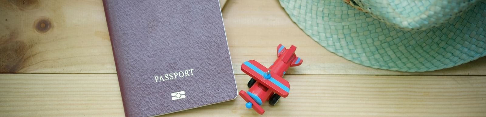 Passport with a toy airplane and hat on a wooden table, symbolizing international travel planning and adventure.