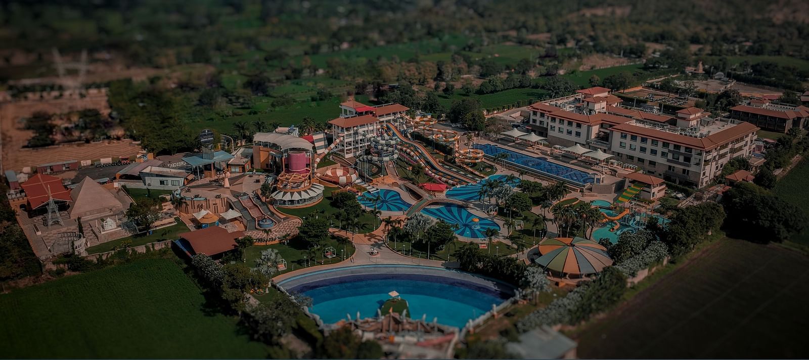 Aerial view of a large amusement park with roofed buildings, set against a dimly lit backdrop - Crescent Resorts