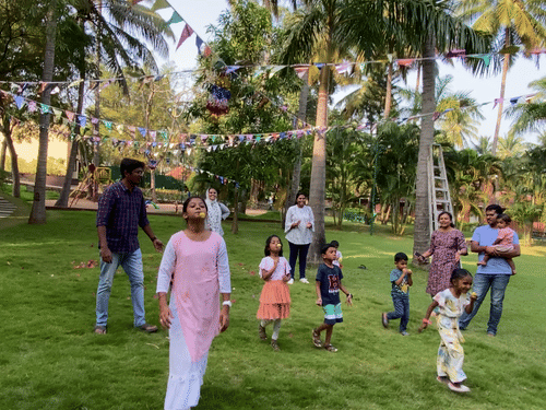  A group of people, including adults and children, are standing on a lush green lawn surrounded by tall palm trees.