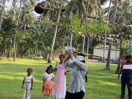  A group of people, including adults and children, are standing on a lush green lawn surrounded by tall palm trees.