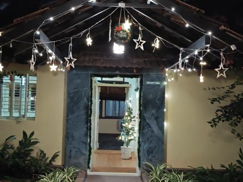 A vertical image showing the lighted entrance of a building at night, with a path leading to an open doorway, decorated with string lights.