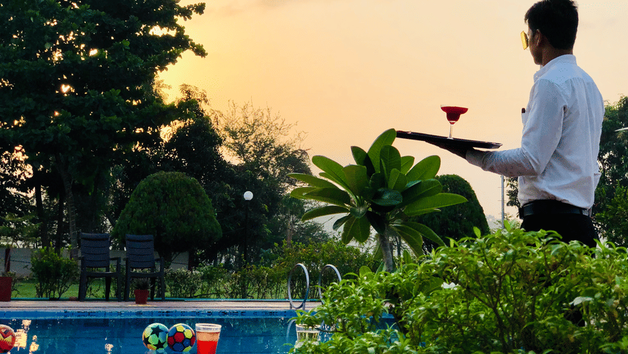 A waiter holding a drink, standing next to the swimming pool during the evening at VITS Kamats Resort, Silvassa.