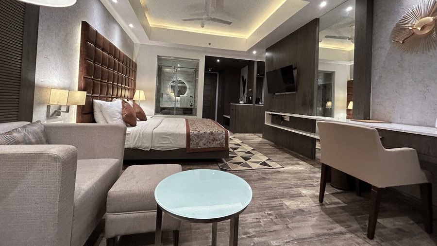 An interior view of a hotel suite showing a seating area with a round table, a desk, and a bed in the background