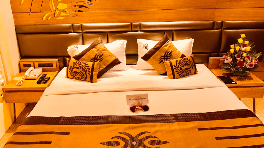 A Club Room at JRD Pride - Business Hotel featuring a neatly-made bed, matching cushions, an orange runner, and nightstands on either side of the bed.
