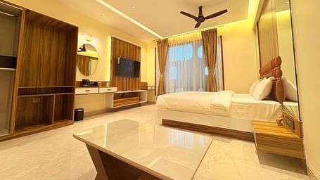 Side view of the bedroom featuring a wall-mounted television, a king size bed, and a window covered by curtains at Hotel Mumbai House, Vashi.