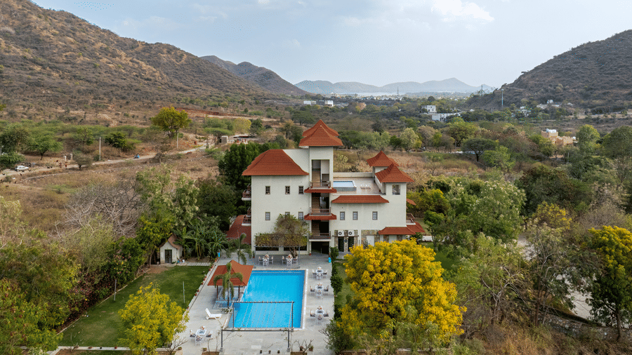 Side view of The Hunting Lodge, Udaipur, featuring a large outdoor swimming pool in the property.