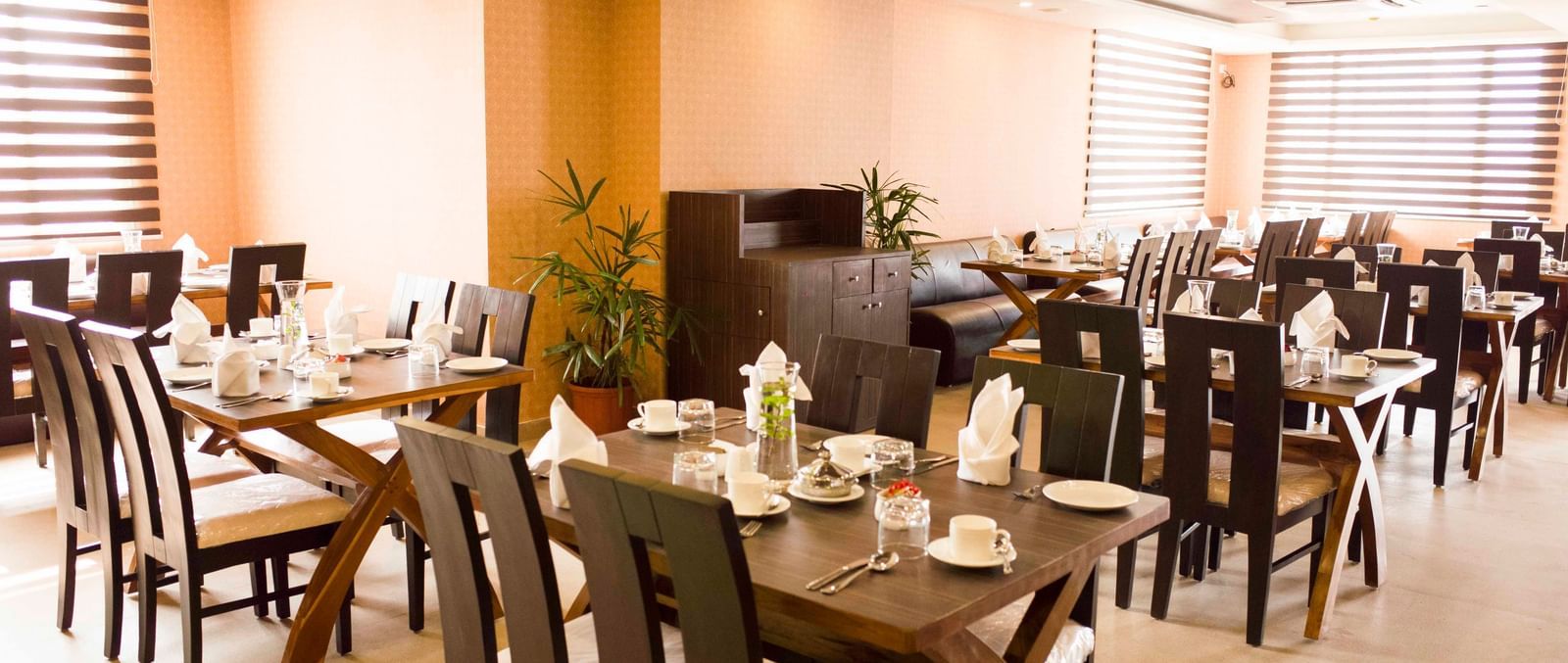 A hotel restaurant dining area with tables set and brown chairs | Daksh The Madhuvan Suites