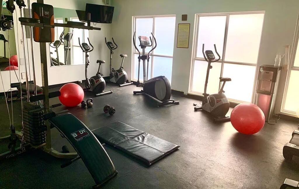 An empty fitness center with various exercise equipment, including weights and treadmills | Altamont Court, Jamaica