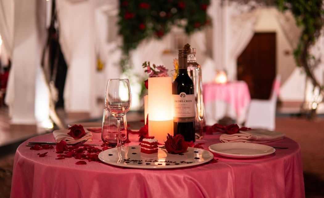 A romantic dining arrangement with a candle and a bottle of wine placed on a table with a dark pink table cloth - Saraca Hotel, Lucknow,