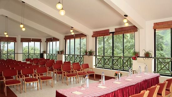 Interior view of a conference or meeting room with large windows, pendant lighting, and red chairs arranged around a long table - Abad Copper Castle, Munnar
