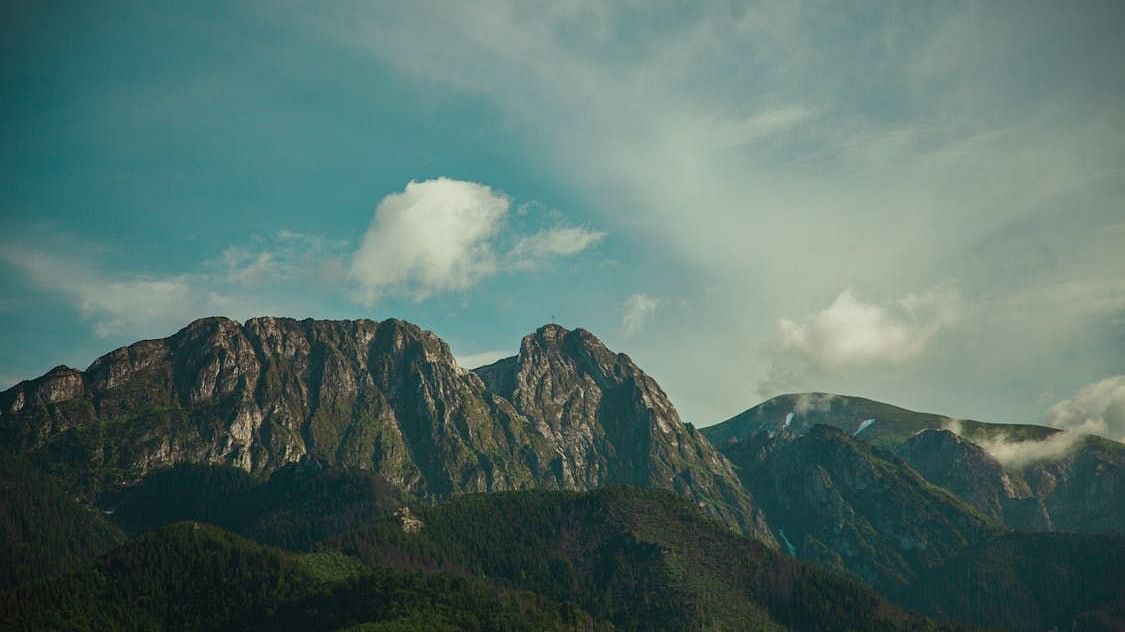 Majestic mountain landscape under a partly cloudy sky, featuring dramatic rocky ridges and lush green foothills.
