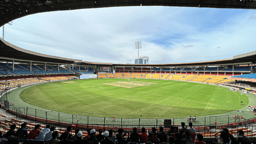 The spectator seating area featuring a cricket match taking place on the green outfield of M. Chinnaswamy Stadium under open skies.