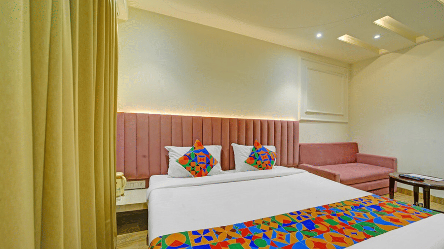 Bedroom with double bed, yellow curtains, wall-mounted TV and sofa seating at Hotel Maurya, Bhopal.