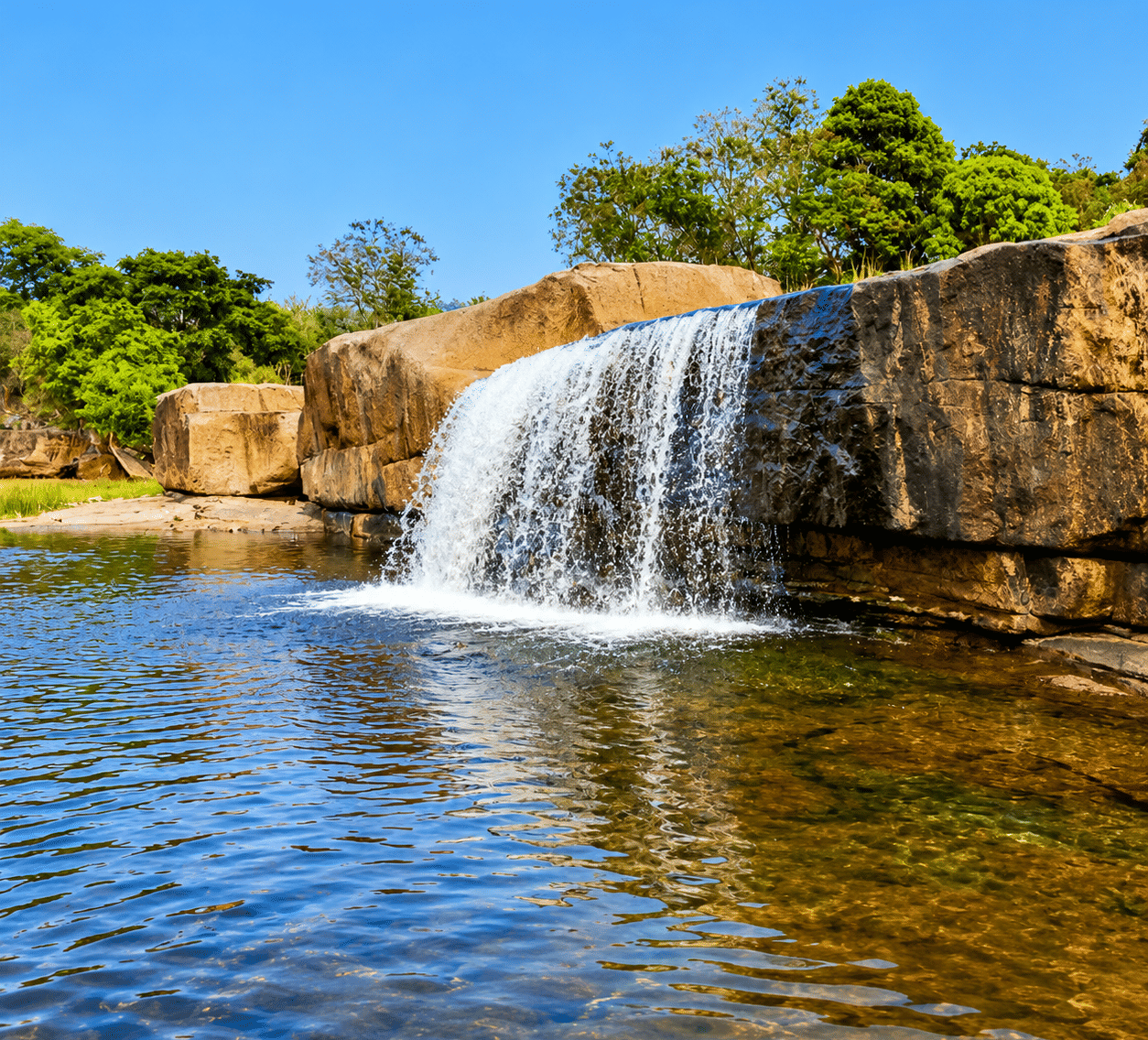 Khasada Waterfall flowing over broad sandstone boulders into a clear shallow pool fringed by trees, near MAYFAIR Palm Beach Resort, Gopalpur-on-Sea.