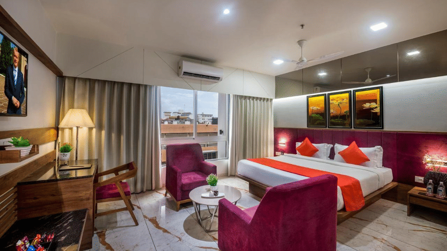 A double bed room with AC, work desk, TV,  windows with curtains and seating table and chair with appropriate lighting