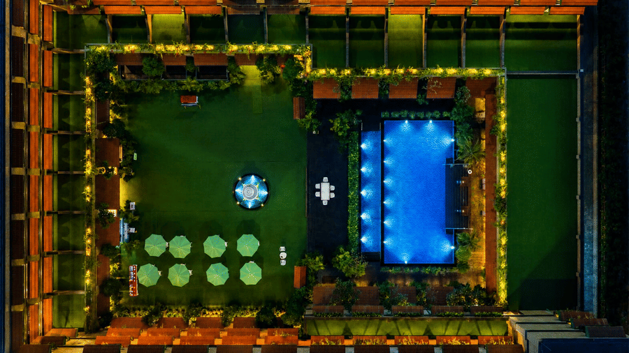 Aerial view of the courtyard, lawn, and glowing blue pool at night at MAYFAIR Bay Resort, Paradeep.
