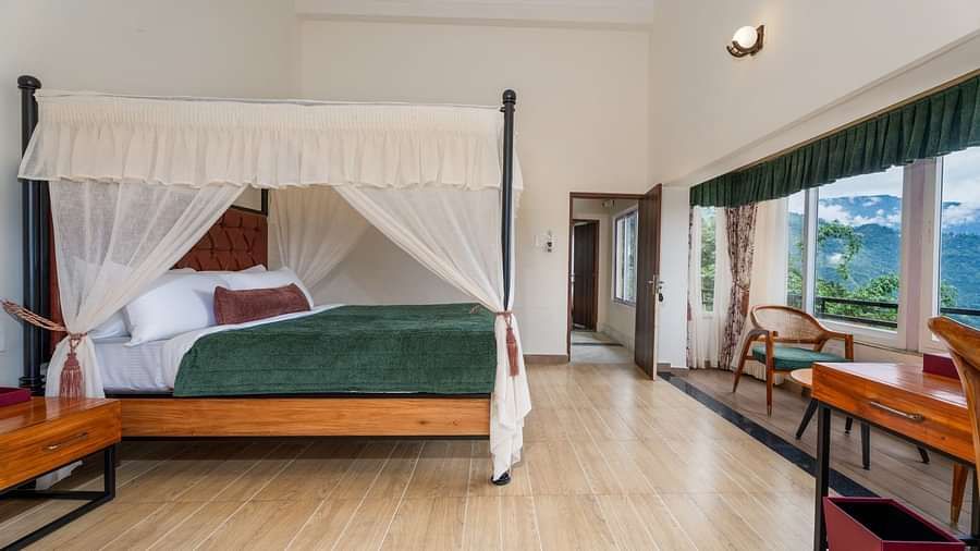  A generously sized bed with curtains on the sides, accompanied by wooden furniture and a breathtaking mountain view through the large windows.