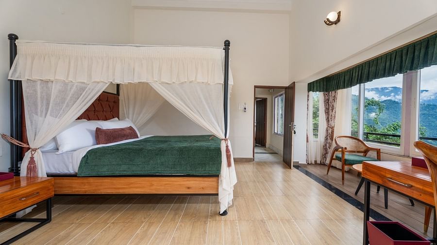  A generously sized bed with curtains on the sides, accompanied by wooden furniture and a breathtaking mountain view through the large windows.