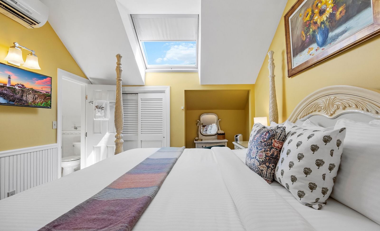 A room with double bed with designed pillows on top, wall art, and cozy yellow decor at Hartstone Inn.