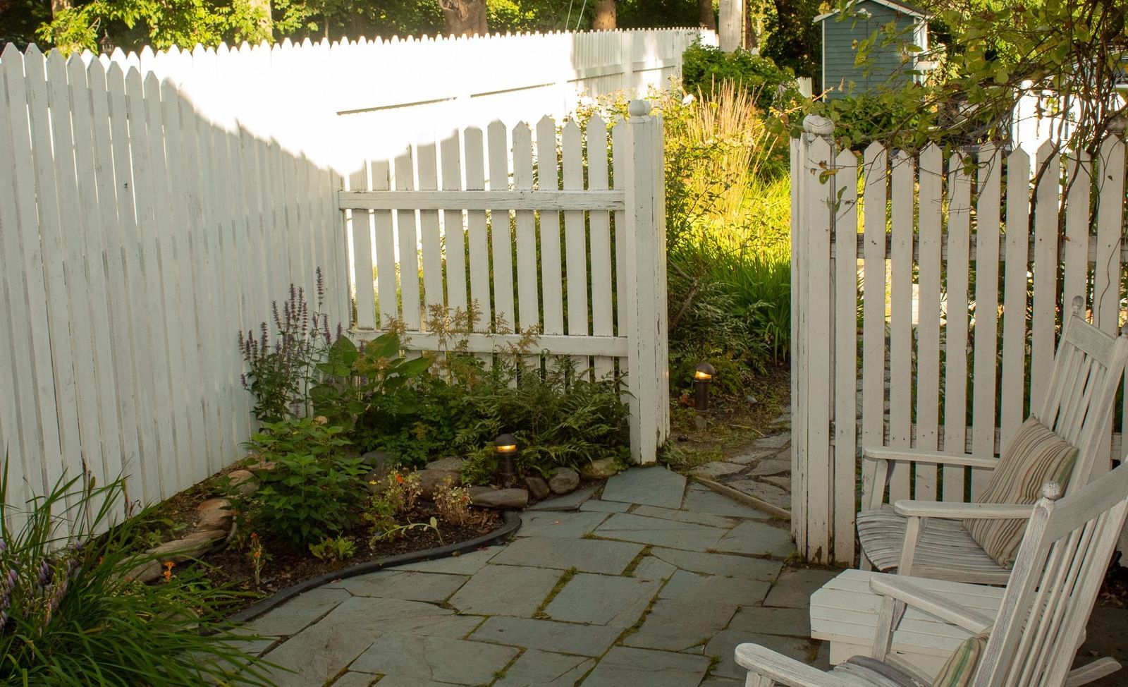 Private garden patio at Hartstone Inn with white picket fence, stone path and wooden bench seating.