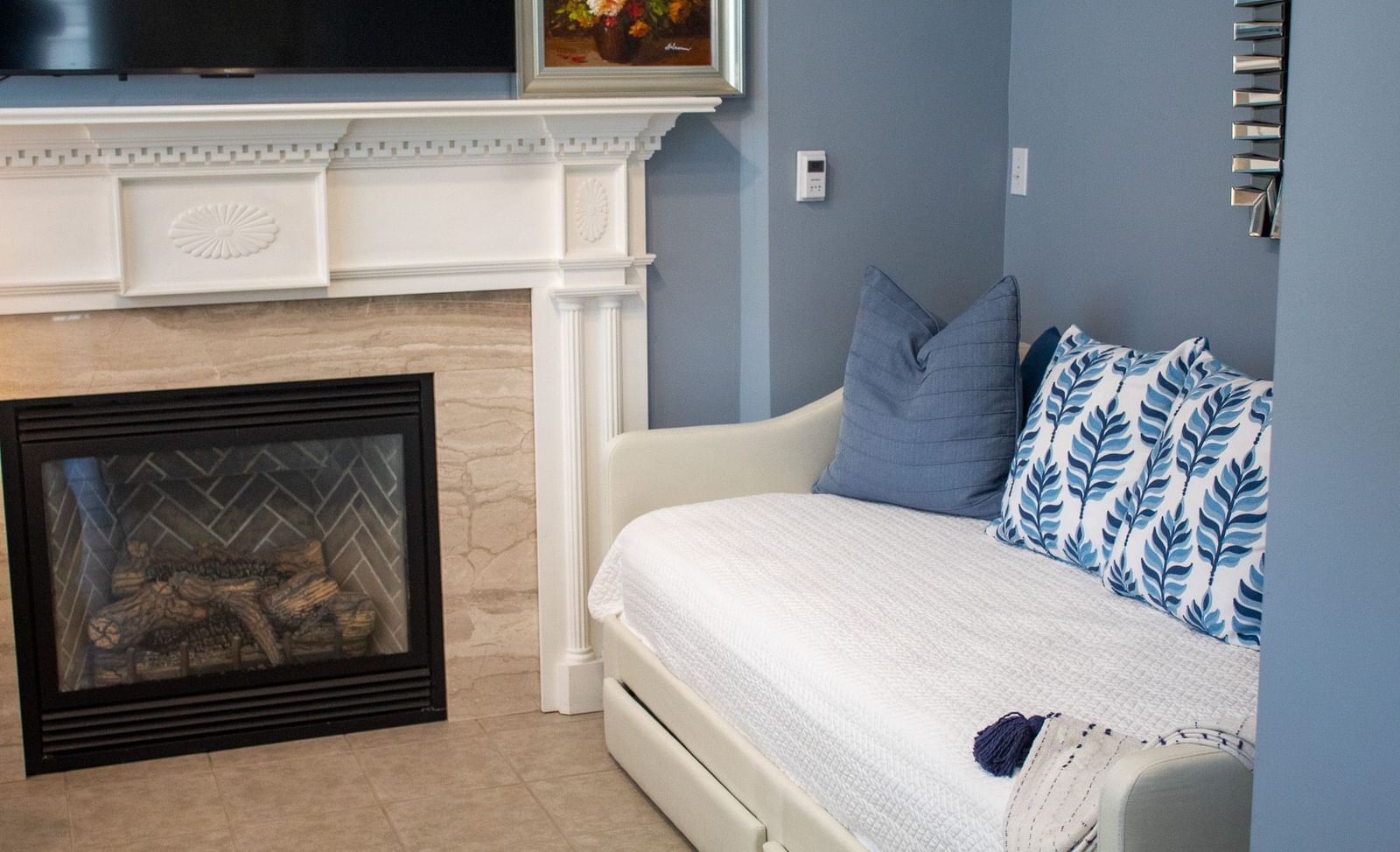 Reading area with white daybed, blue pillows, fireplace with white mantel and TV above at Hartstone Inn.