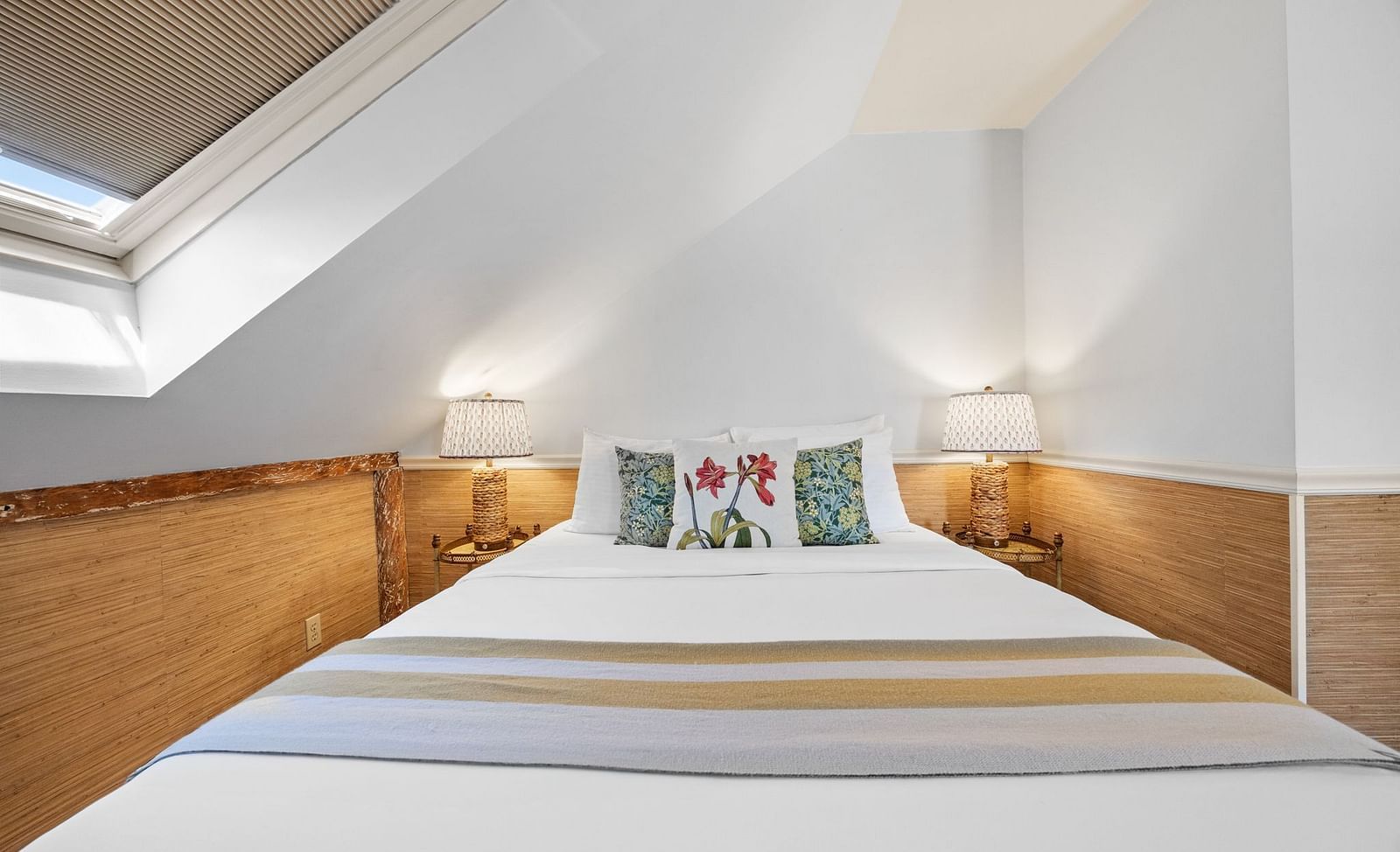 A bedroom with sloped ceiling with floral bed pillows at Hartstone Inn