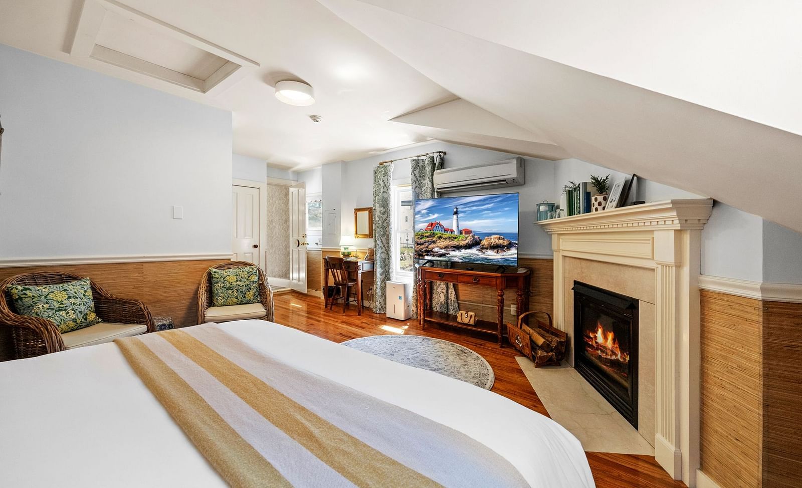 A room with king size bed, fireplace, a pair of chairs placed near the bed and a tv at Hartstone Inn.