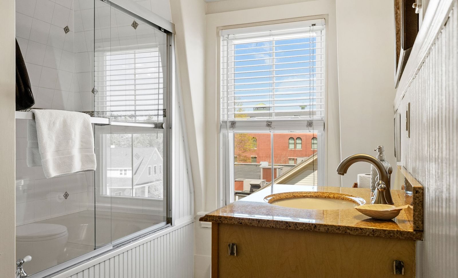 Compact bathroom with window view, white fixtures, and tan vanity at Hartstone Inn