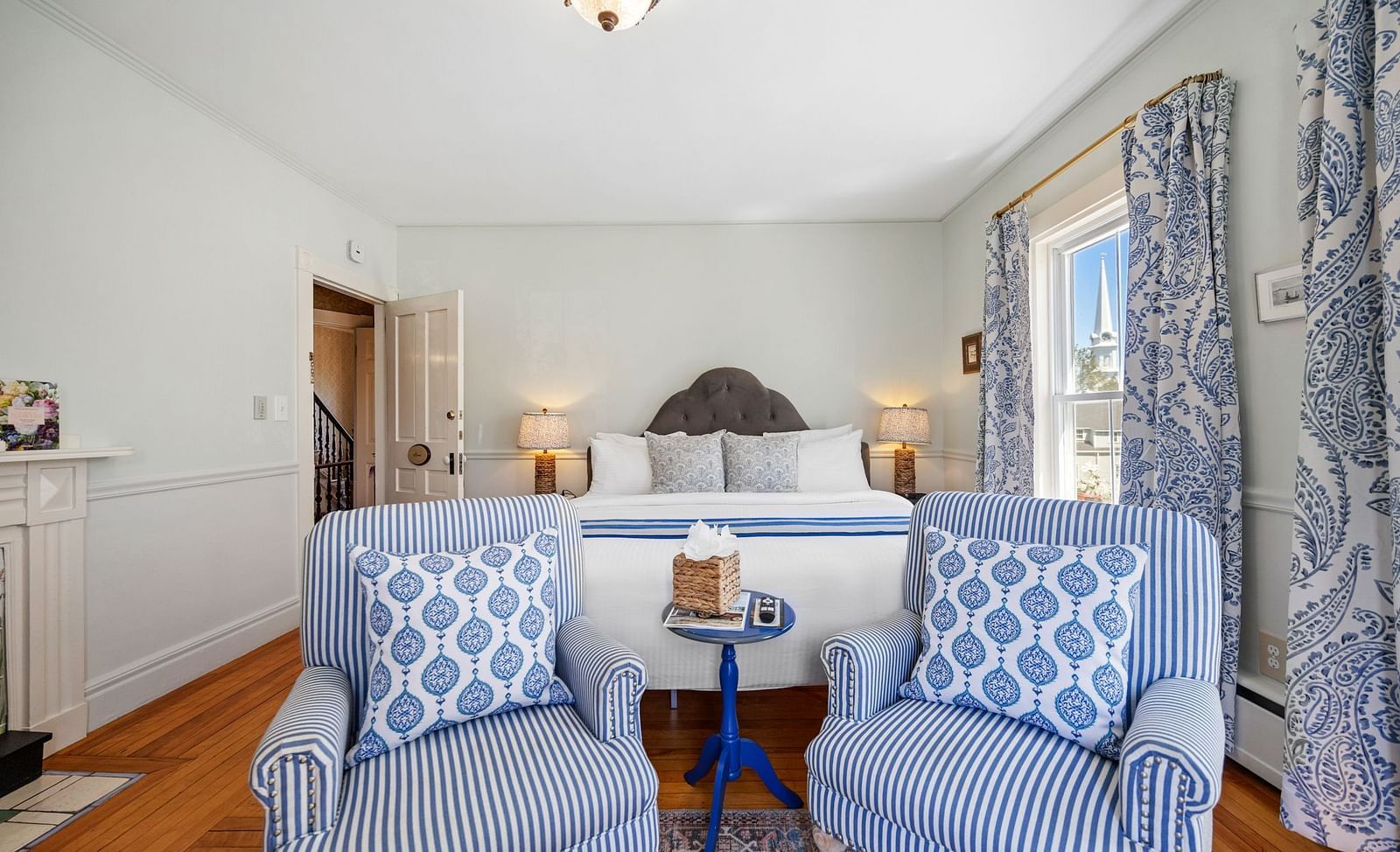 Seating area with blue patterned chairs, round table and showcasing queen sized bed in the background at Hartstone Inn