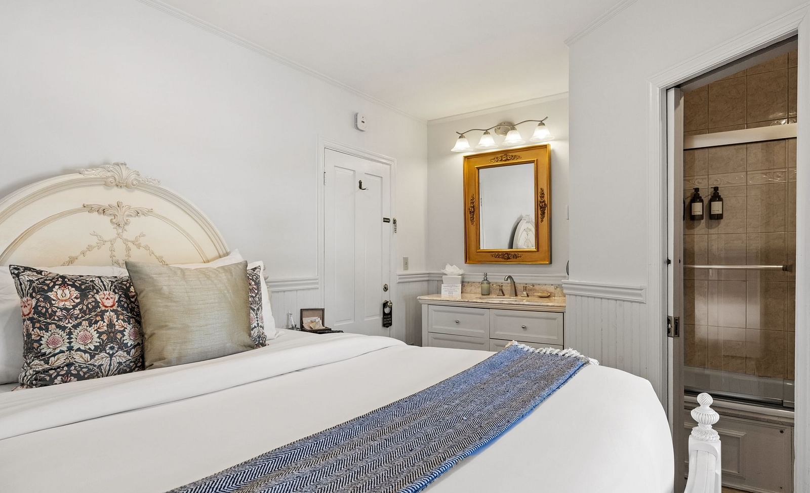 A bedroom with ornate headboard, a mirror, table and blue-accented runner at Hartstone Inn
