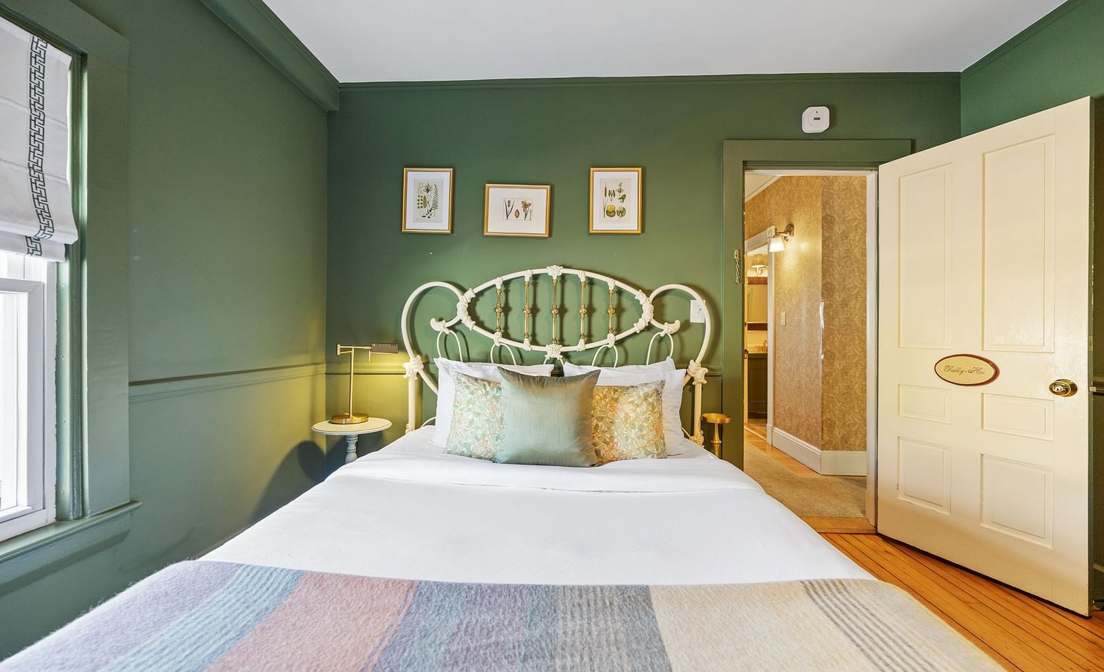Green-walled bedroom with white iron bed with framed arts in the wall at Hartstone Inn.
