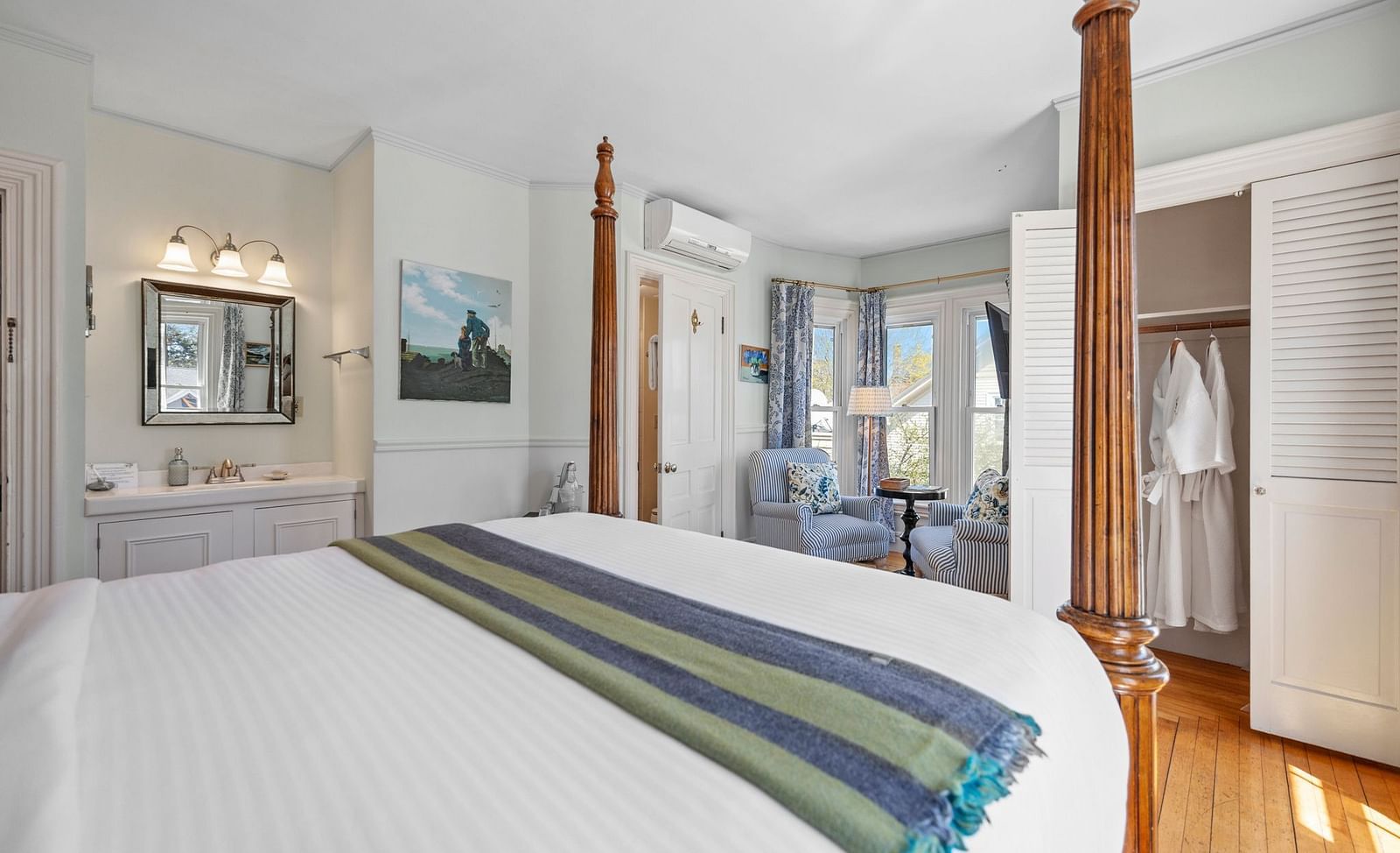 Elegant guest room with canopy bed, a closet hanging a pair of bathrobe and a sitting area in the corner at Hartstone Inn
