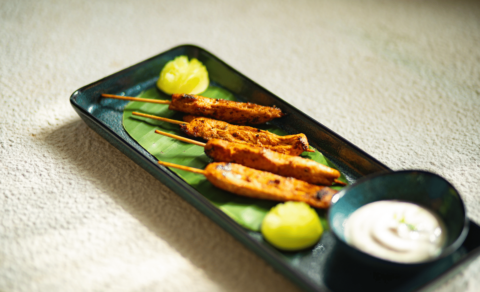 A plate of grilled chicken skewers with lime wedges and a side of sauce at Stanley Revelation.