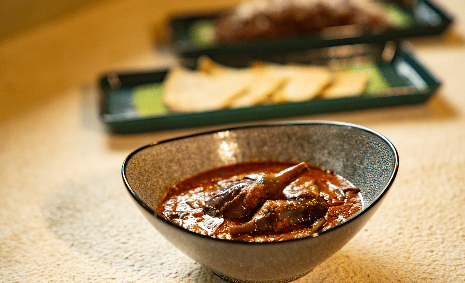 A bowl of rich, dark meat curry at Stanley Revelation, with other dishes blurred in the background.