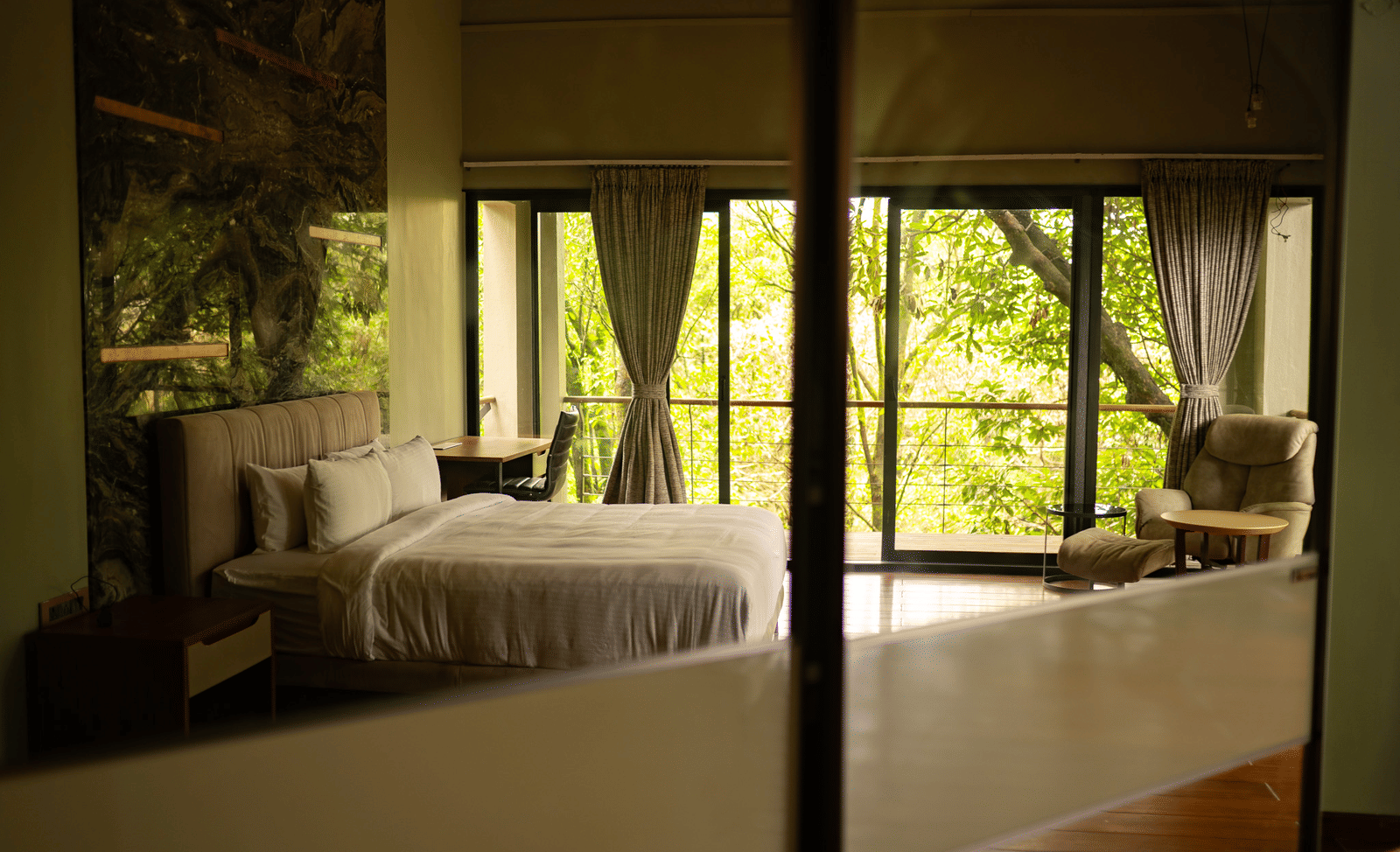 A bedroom at Stanley Revelation with a large bed, seating, and a balcony overlooking a forest.