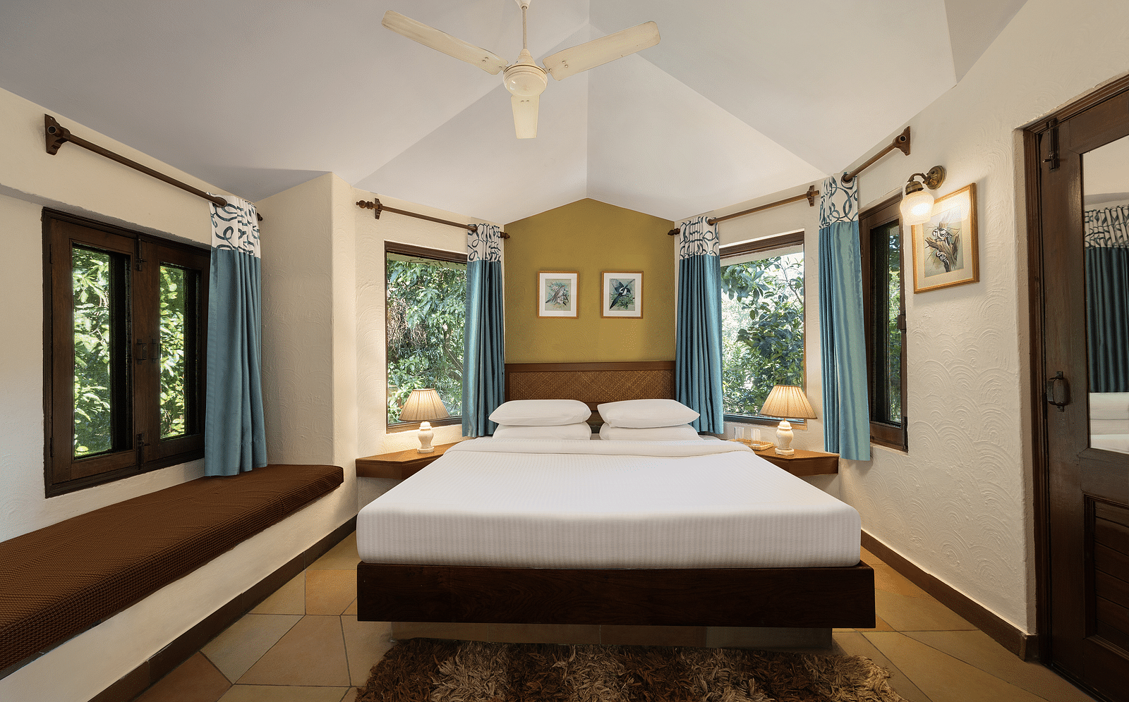 An image of a bedroom with double size bed, bedside table on either side, photos hanged on the wall and four windows from which natural lights are coming in - The Riverview Retreat,  Corbett