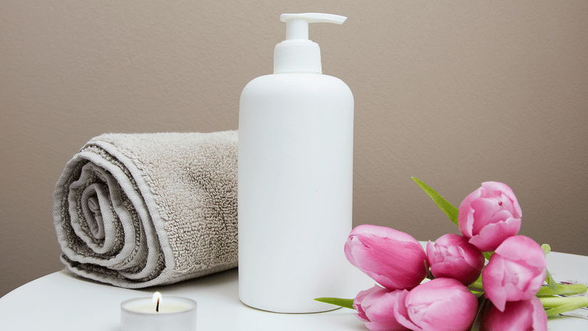 A bunch of tulip flowers kept next to a bottle and a rolled towel by a tealight candle