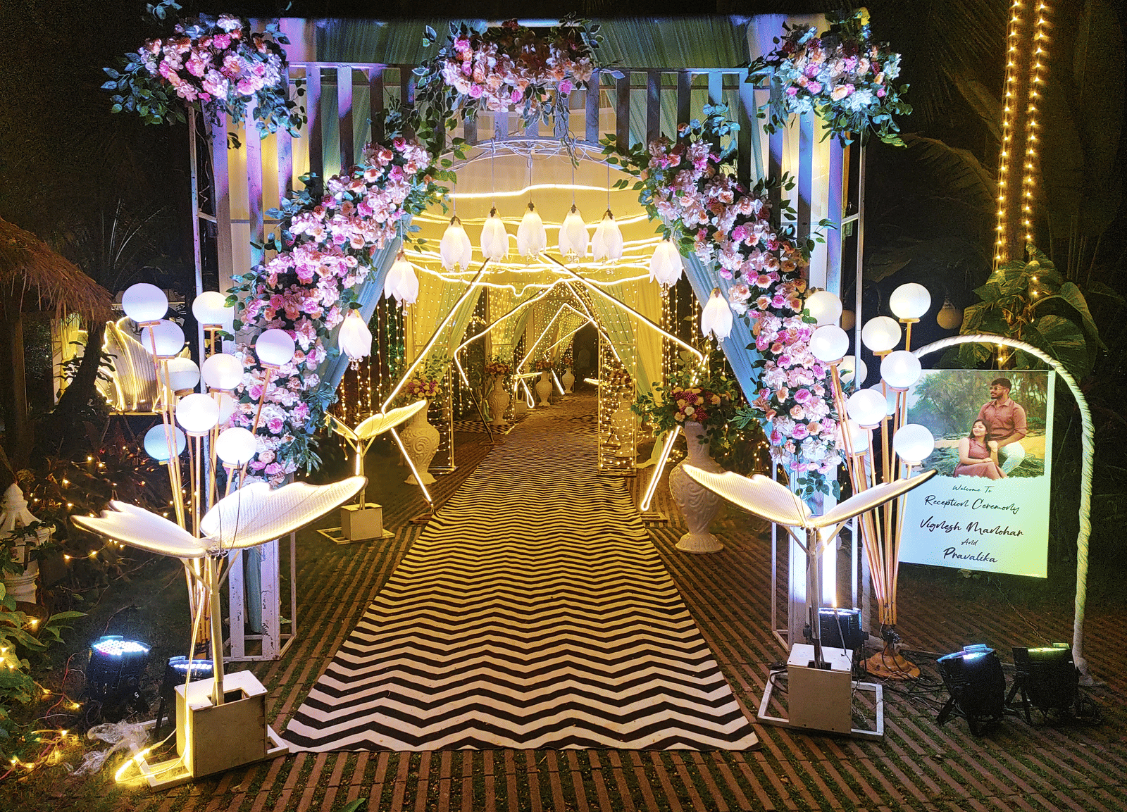 Entrance arch decorated with pink and white flowers and lights at Paradise Lagoon Resort, Udupi.