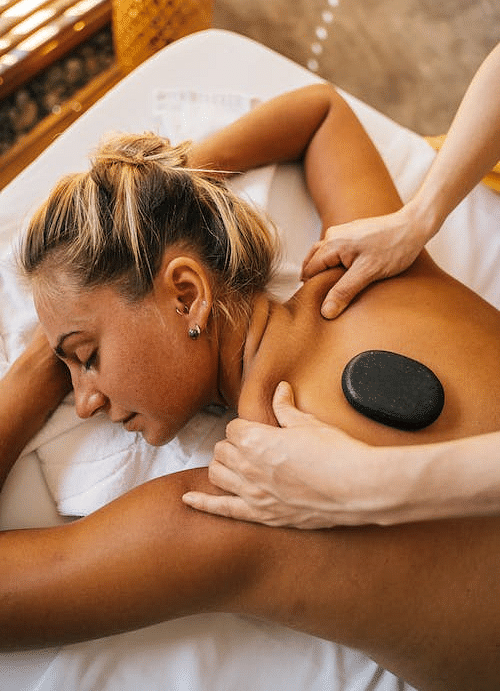 A woman lying on her stomach receiving a back massage with a piece of stone