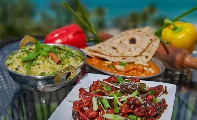 Variety of Indian dishes with vegetables, bread, and chutney, placed outdoors with a sea view | A Stone's Throw Away
