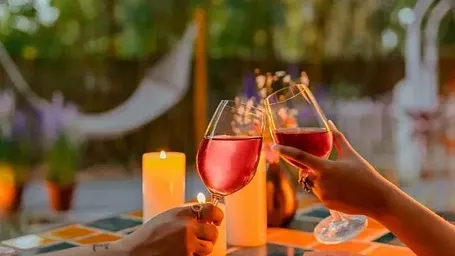 Close-up of two people toasting glasses of rosé wine at an outdoor table with a candle at Karma Chalets.