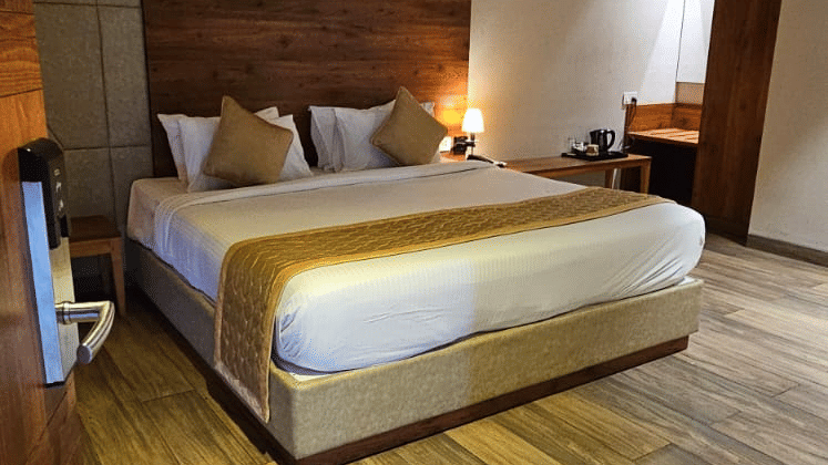 Double bed with wooden headboard and matching floor panel at Cholaa Dynasty, Kumbakonam.