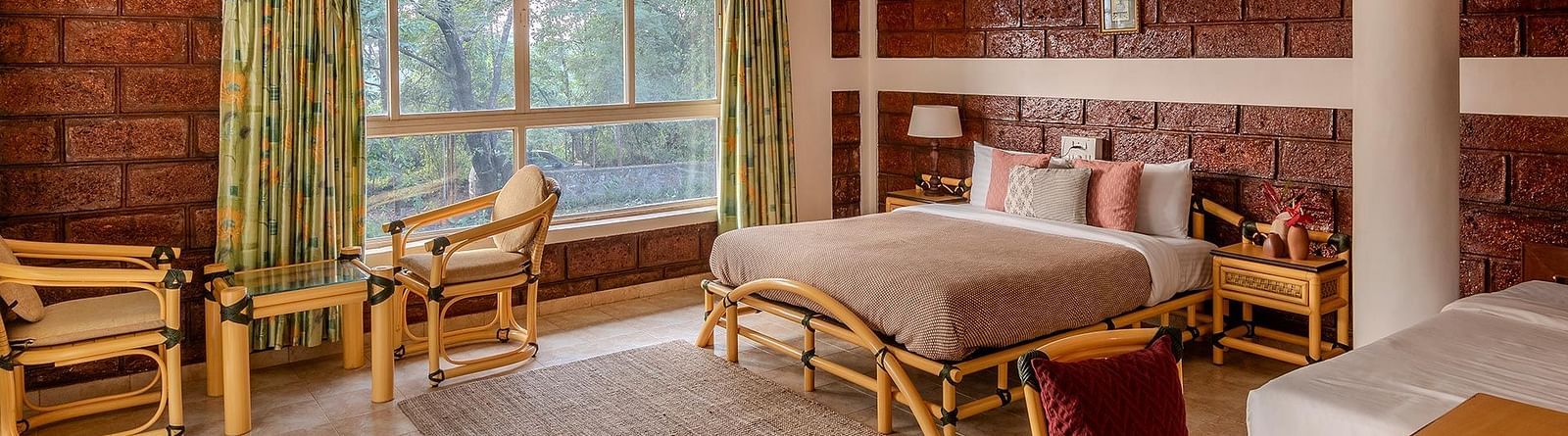 A side view of a double bed room with a side table, wooden floor, rug, pillar, chairs, table and windows with curtains