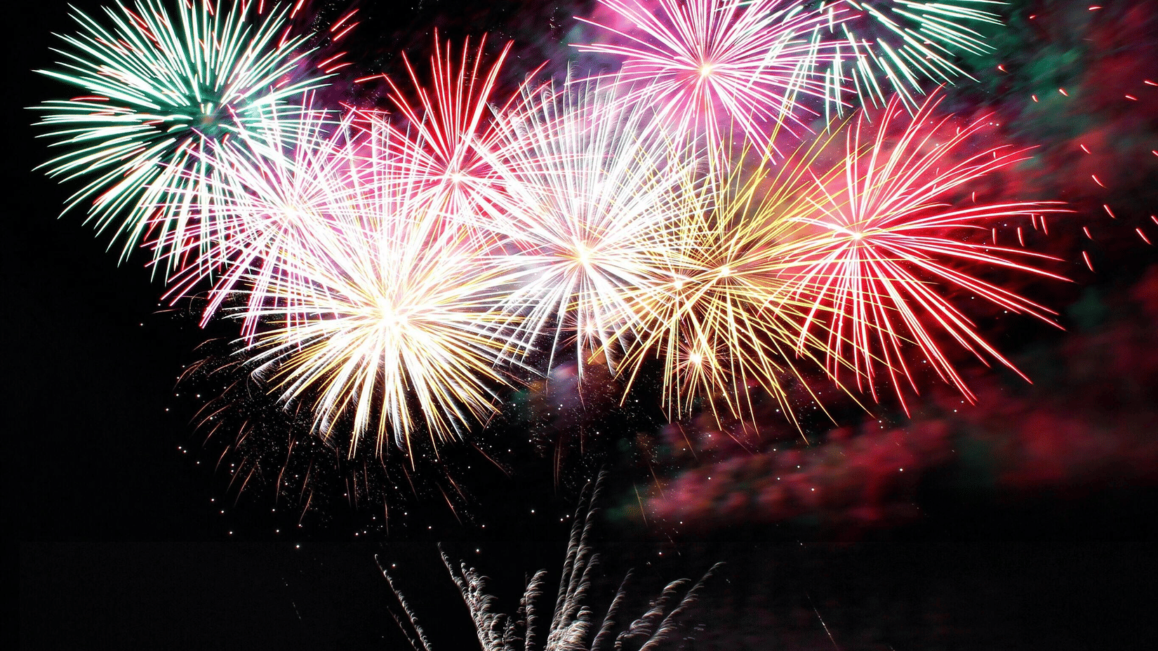 Colourful fireworks lighting up the night sky over a distant stage.
